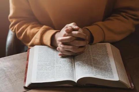 Hands folded in prayer over an open Bible