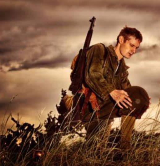 A soldier resting on a hillside at sunset, helmet in hand
