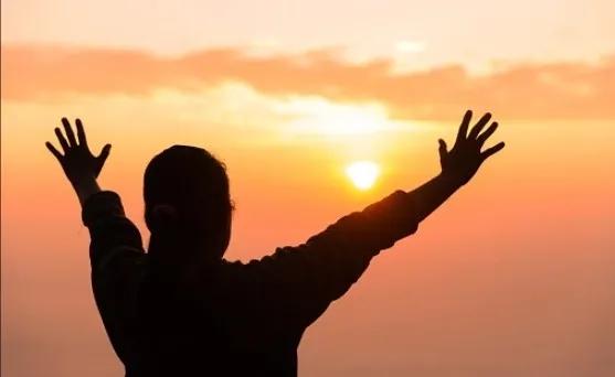 A silhouetted figure raising both arms towards a sunrise